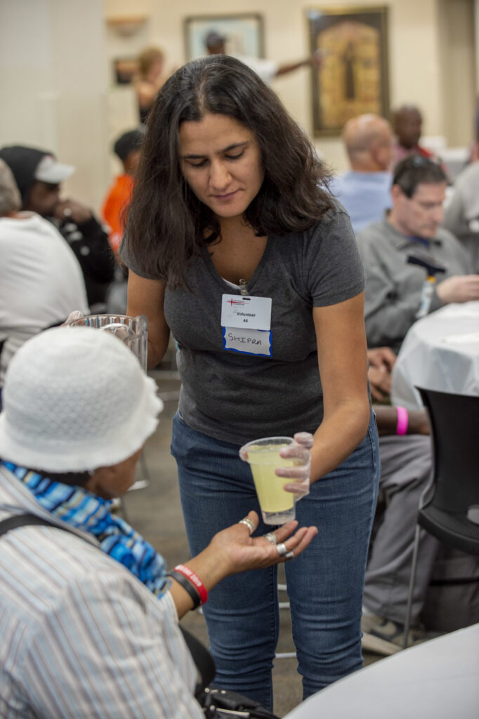 Person with name tag handing a drink to a person sitting down.