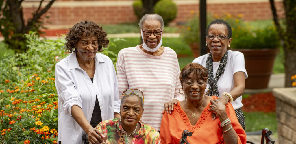 Five sisters posing for a photo; three are standing and two are sitting.